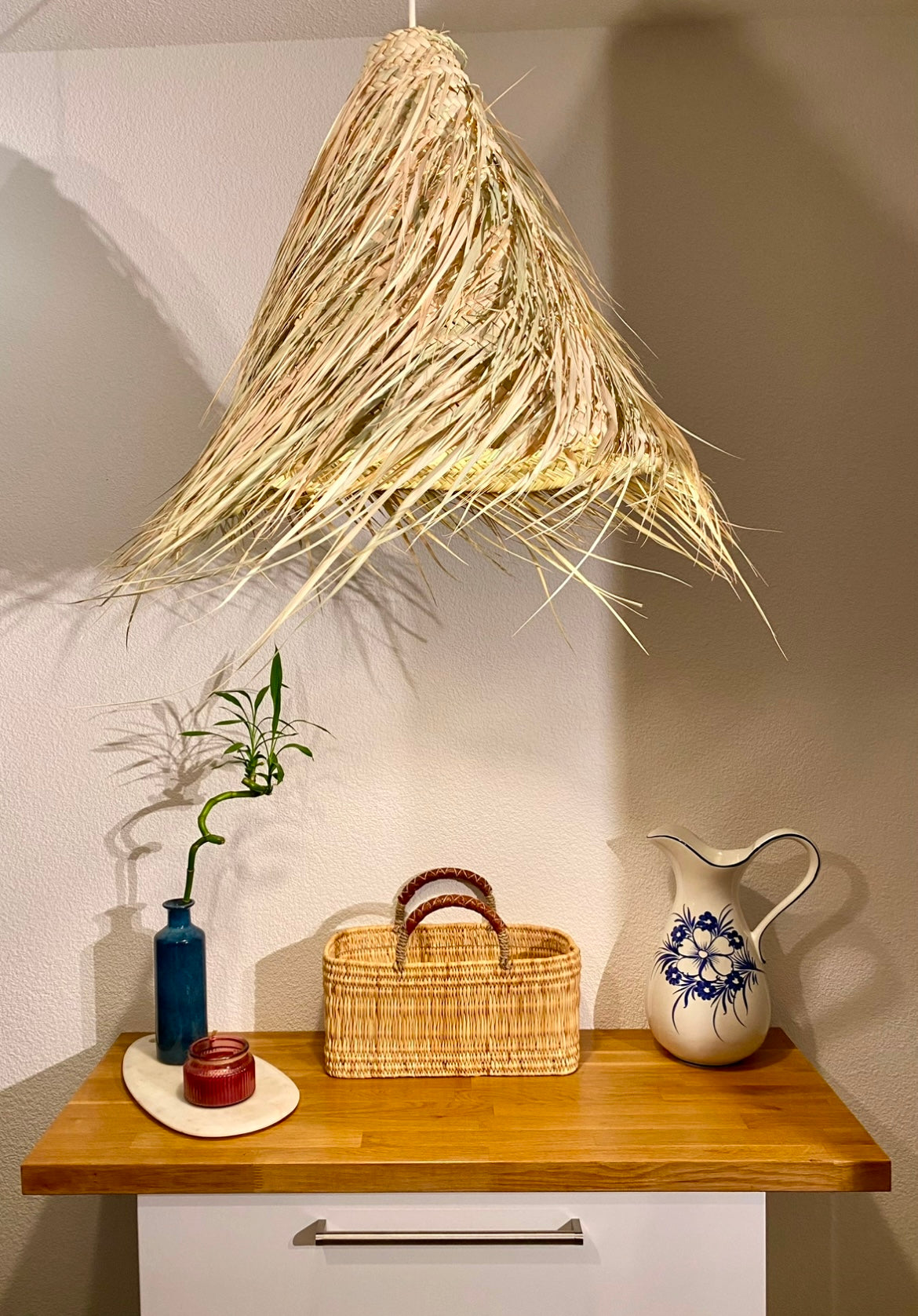 Étagère en bois élégamment décorée, mettant en valeur une collection de paniers artisanaux marocains en feuilles de palmier. La scène inclut également des vases en céramique, un miroir rond encadré de raphia, et une suspension en fibres naturelles.